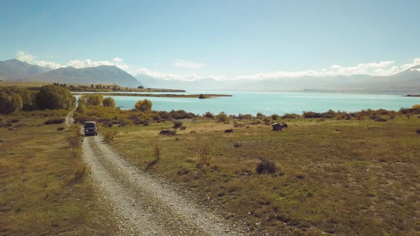 Aerial: A static camera shot of a camper van going on gravel road with a lake Tekapo in the background in South Island of New Zealand