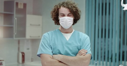 Young dentist man or doctor in the hospital closeup looking straight to the camera and take off the surgical mask and happy smiling large , he have a perfect white teeth and charismatic face.