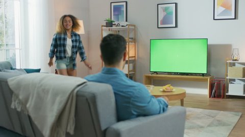 At Home: Girlfriend Joins Her Boyfriend on a Couch, They're Watching Green Chroma Key Television Screen. Couple Watching Movies, TV Shows, News.