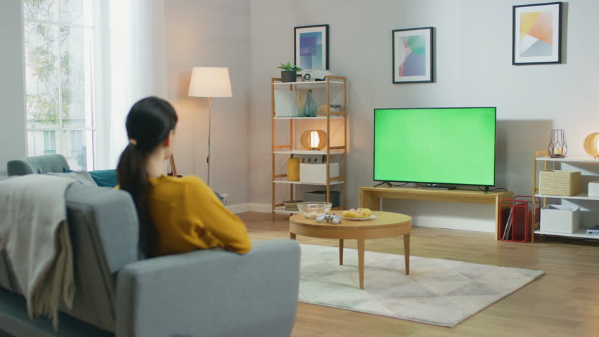 Girl Sitting At Home Sitting on a Couch, Watching Green Chroma Key Screen, Relaxing. Man in a Cozy Room Watching Sports Match, News, Sitcom TV Show or a Movie. Royalty-Free Stock Footage #1022993827