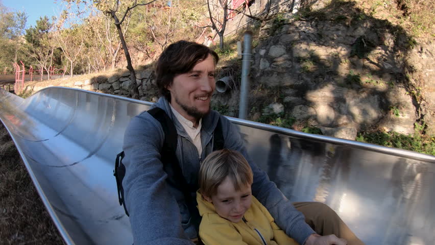 Slowmotion shot of a father and son riding down the alpine roller coaster in an autumn forest