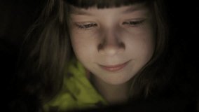 Night shot of kid's girl face browsing tablet pc with light reflection on it