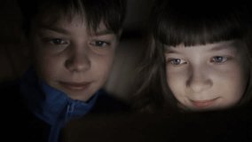 Night the faces of the children , brother and sister browsing a tablet PC with the reflection of light on them