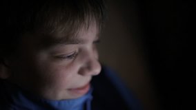Night shot of the boy's face looking at a tablet PC with light reflection on it