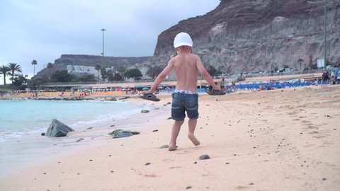 A little boy runs along the sandy beach along the coast and runs away from the sea wave