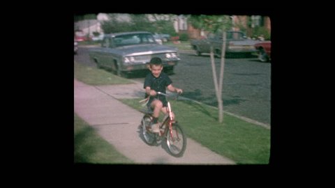 1964 Cute little boy rides bike next to vintage cars