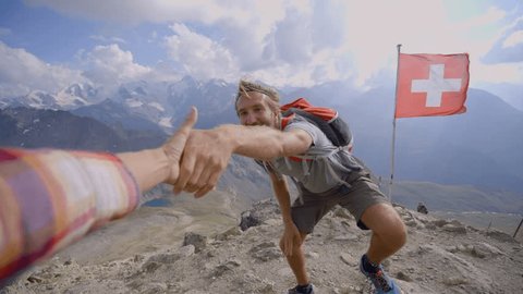 Point of view of hiker pulling out hand to help teammate reach the summit. Young man hiking in the Alps, hand reaches out to help. Helping hand concept. Achievement and success at mountain top.