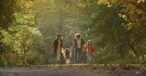 Young asian family of four walking down the road in golden autumn park, cheerfuly smiling - 4k