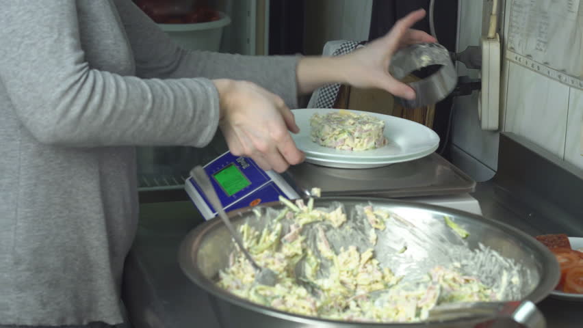 A cook in the kitchen weighs portions of salad on scales in grams and serves to the table, weigher