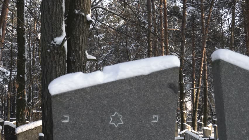 snowy tombstones with Star of David at a jewish cemetery or graveyard in winter in forest
