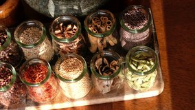 Various spices in glass jars on wooden table. Panning to the left, selective focus.