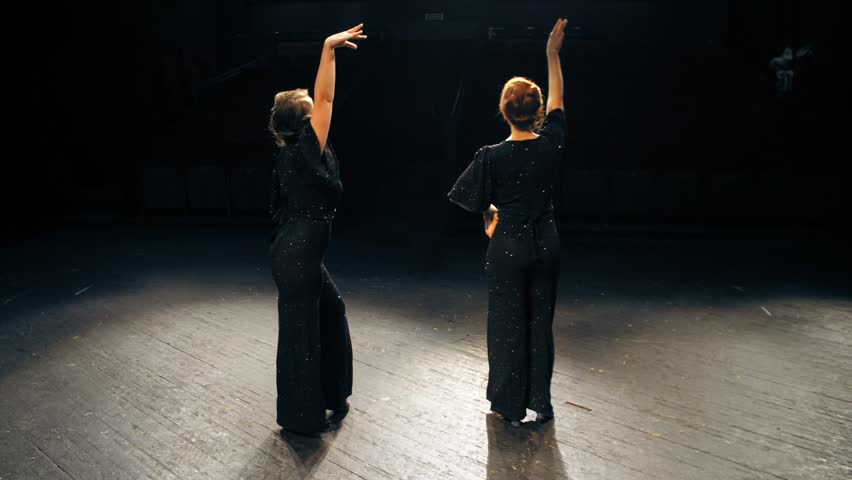 Two women in black leave theatrical scene in the dark. The end of the play