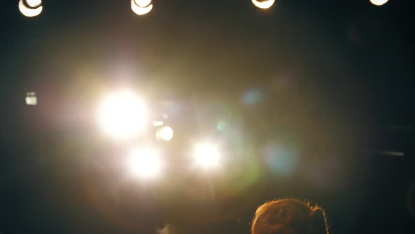 Woman in black dancing professionally in theatrical light. Back view