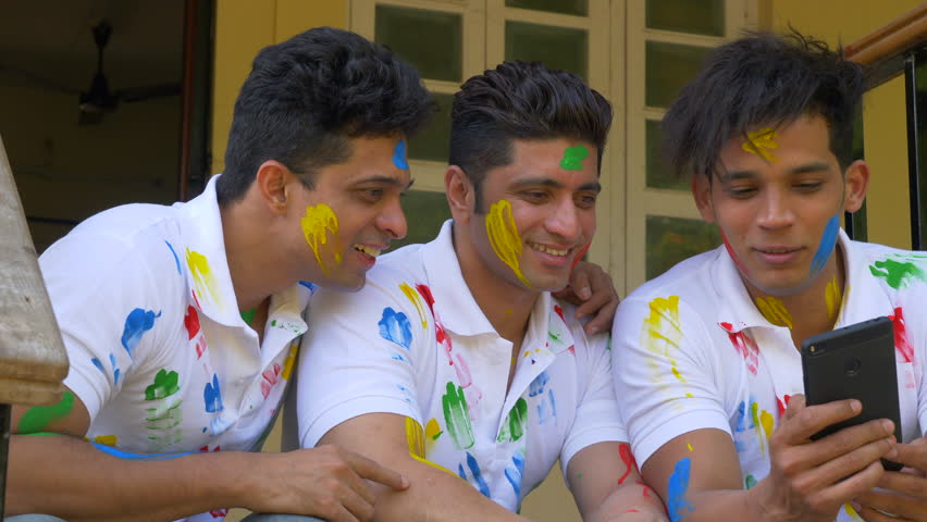 Young boys enjoying Holi festival of colours and using tab in India.