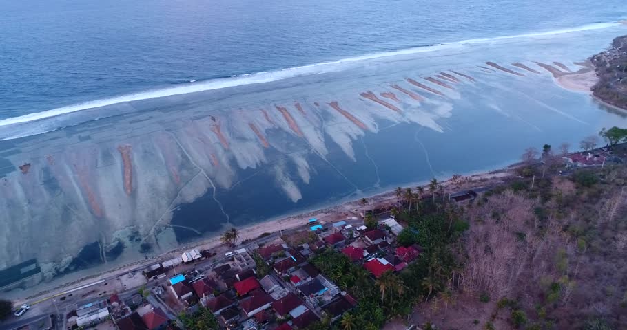 Drone footage of Nusa Penida, Indonesia with small village built on the east coast, waves are breaking over the pristine shallow coral reef and the algae cultures growing. 