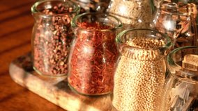 Various spices in glass jar on wooden table. Panning to the right. Selective focus.
