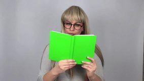 Caucasian blonde woman holding and reading book isolated over grey background in studio