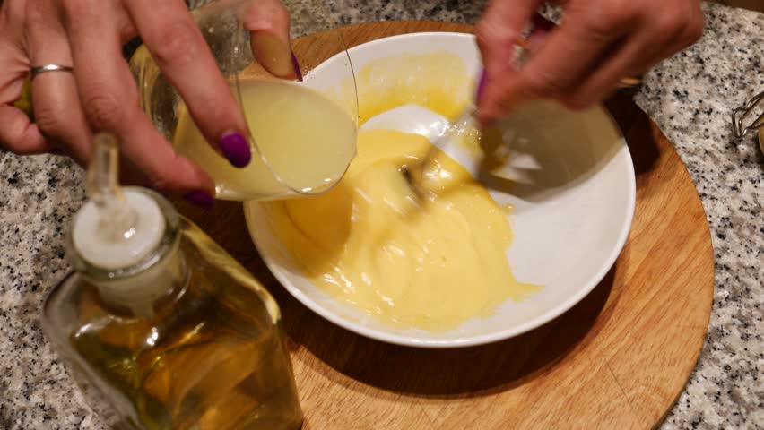 Female hands preparing homemade mayonnaise with egg yolk, lemon juice and olive oil