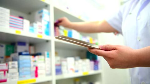 Pharmacist holding computer tablet using for checking medication details on a box in pharmacy drugstore.