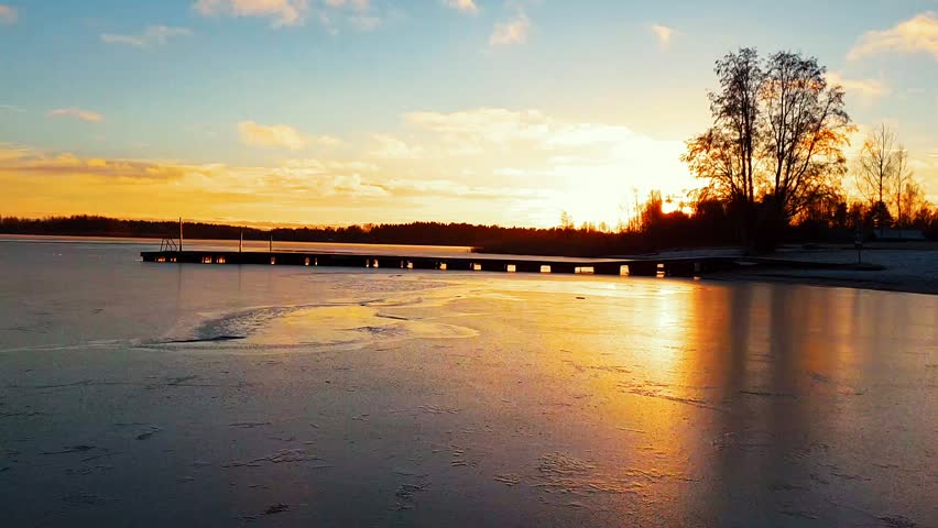 timelapse of jetty dock and golden sunset in the winter, water making the thin ice pulsate and jump