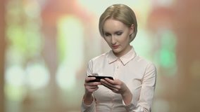Smiling office woman using mobile phone. Attractive blonde woman in office shirt playing video game on abstract blurred backgroud.