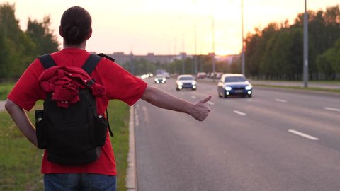 Hitchhiking man with backpack stand thumb up on roadside, try to catch car on road