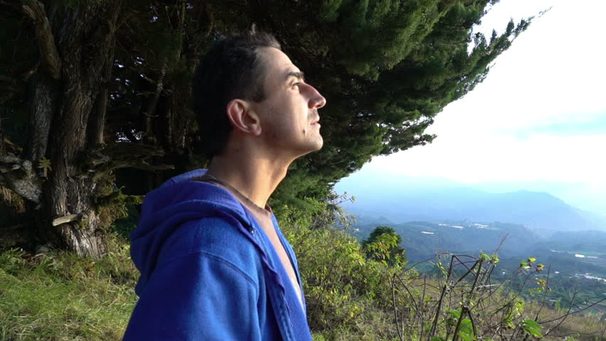 Man standing in mountains landscape and looking high in the sky searching. UFO hunter