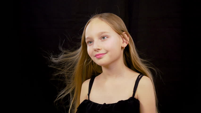 Wind blowing on girls face. Close up, cute adorable little model caucasian girl with fluttered hair looking sidewards, isolated on black background
