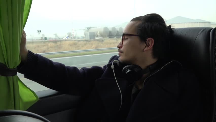 A young asian european man watches out of the flixxbus, while he passes the Schiphol Airport.