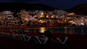 Playa de las Americas holiday resort on Tenerife Canary Island shines with night lights reflected in waves of Atlantic ocean.
