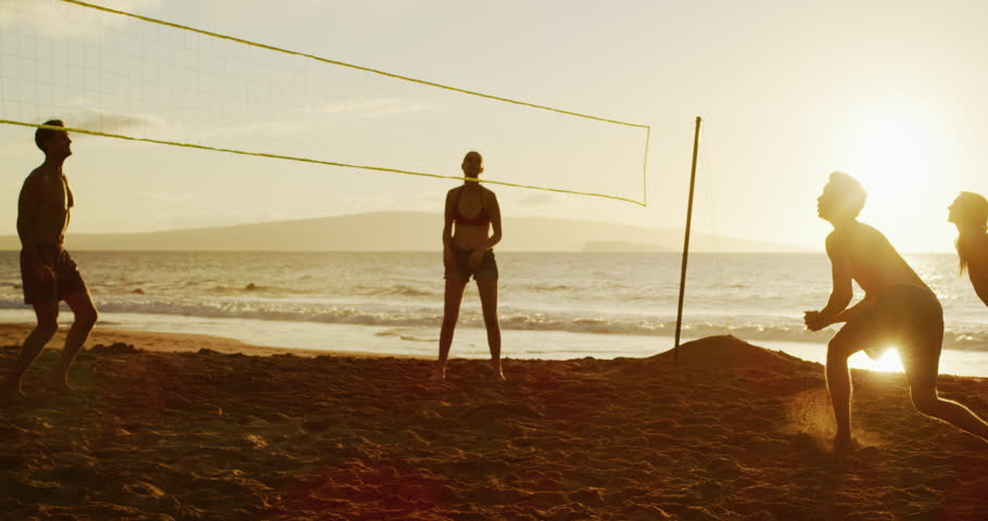 Group of friends playing beach volleyball at sunset, athletic man dives to save volleyball, slowmotion