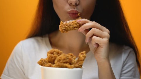 Girl eating chicken wings, high calorie food and health risks, cholesterol