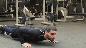 Athletic muscular handsome young man with beard in black sportswear exercising in gym, doing push-ups. Static shot. Training or healthy lifestyle concept.