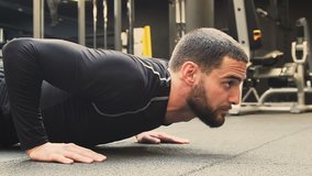 Athletic muscular handsome young man with beard in black sportswear exercising in gym, doing push-ups. Medium shot, side view. Bodybuilding gym training routinehealth concept.