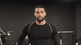 Athletic handsome confident young man with beard in black sportswear looking at camera, crossing arms, changing body position. Medium shot. Confidence concept