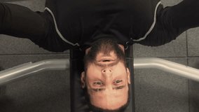 Top view of athletic handsome young man with beard in black sportswear doing bench press with barbell in gym, training hands. Medium shot, static shot. Training concept.