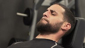 Close up shot of athletic handsome young man with beard in black sportswear exercising hard on leg press machine in gym. Static shot, side view. Training concept.