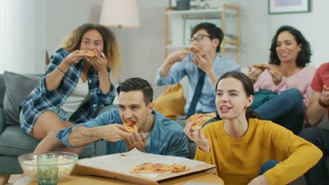 At Home Diverse Group Friends Watching TV Together, They Share Gigantic Pizza, Eating Tasty Pie Pieces. Guys and Girls Watching Comedy Sitcom or a Movie, Laughing and Having Fun Together.