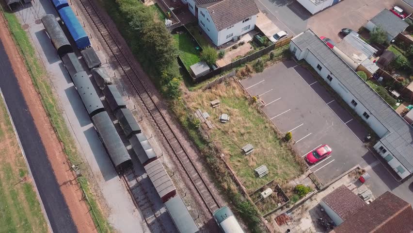 Stationary top down aerial shot of a vintage Diesel engine pulling passenger carriages through a 3 track train station in Washford, Somerset.