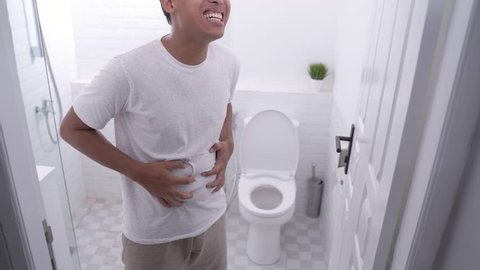 portrait of a man hold his stomach painful. stomach ache and problem. bathroom toilet in the background