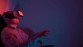 Young man using a VR headset and headphones playing on a virtual synthesizer. Sits in a dark smoke-filled room with colored light.