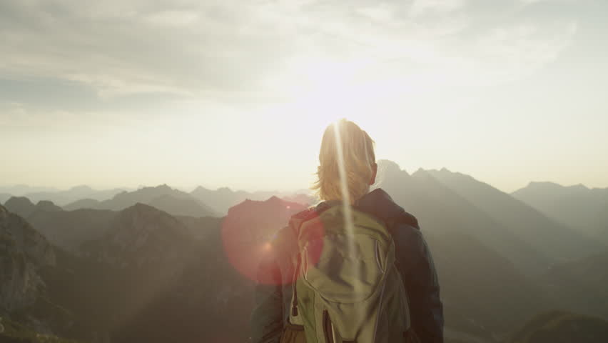 SLOW MOTION, CLOSE UP, LENS FLARE: Trekker girl celebrates reaching the mountaintop with a breathtaking view of the mountain range on a sunny summer day. Unrecognizable hiker woman outstretches arms.