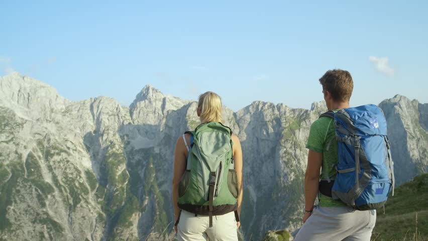 SLOW MOTION, CLOSE UP: Young tourist couple celebrates a successful hiking trip in the picturesque Slovenian Alps. Unrecognizable woman and her boyfriend lifter their arms victoriously after long trek