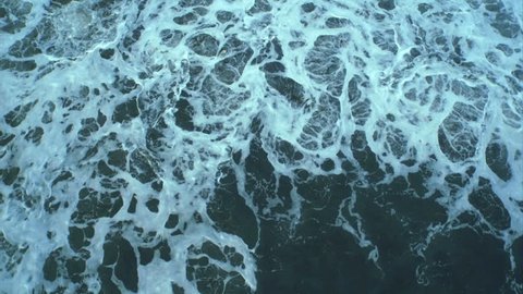 Aerial drone footage of textured pattern formed by white sea foam. Lockdown shot of huge ocean waves crashing on shore. As the waves calm the appearance changes. Overhead perspective. HD 1080 video.