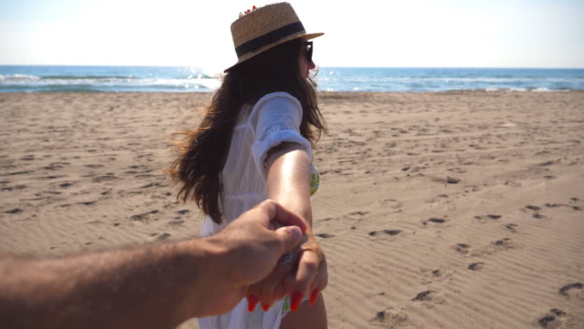 Girl holding male hand and running on beach to the ocean. Follow me shot of young woman in hat pull her boyfriend on the sea shore. Summer vacation or holiday concept. Point of view POV Slow motion | Shutterstock HD Video #1023169255