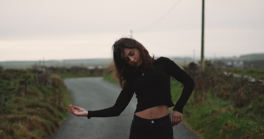 Skinny young lady on the countryside road dacing passionately in front of the camera , she have closed eyes and moving slowly, 4k