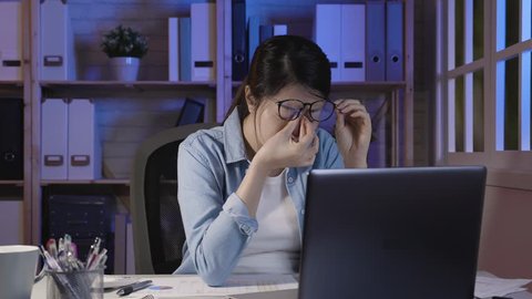 slow motion of beautiful woman working late at home. Tired young white collar female worker rubbing eyes while sitting in front of laptop computer on promising project in house office at night.