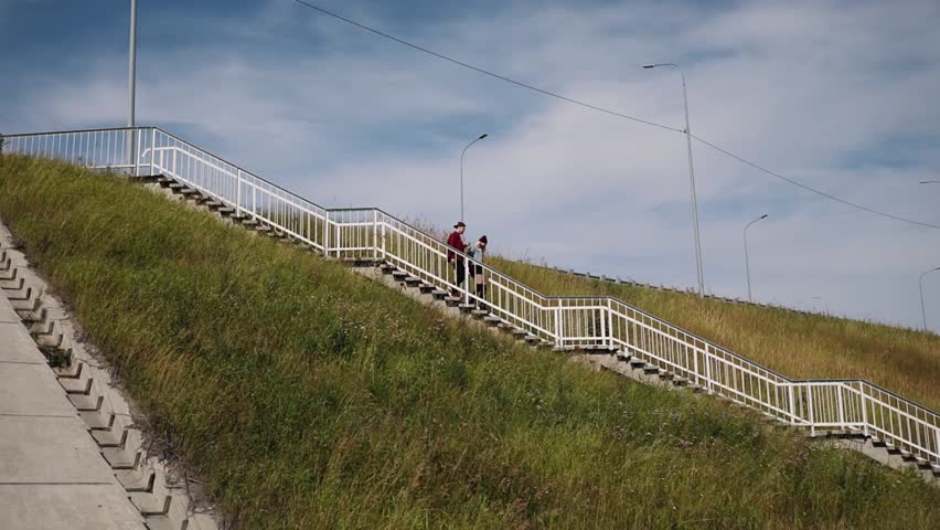 Happy couple, in plaid shirts, holding hands and walking on a car bridge on a sunny summer day.