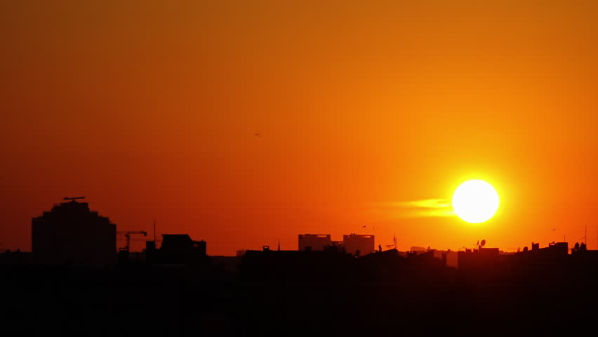 Mid shot time-lapse of the sunset and sun going down over dark rooftops in shadow with a bright orange sky in Istanbul