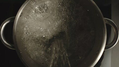 SLOW MOTION: Pure water pouring into a steel pan on black glass-ceramic stove - Top view